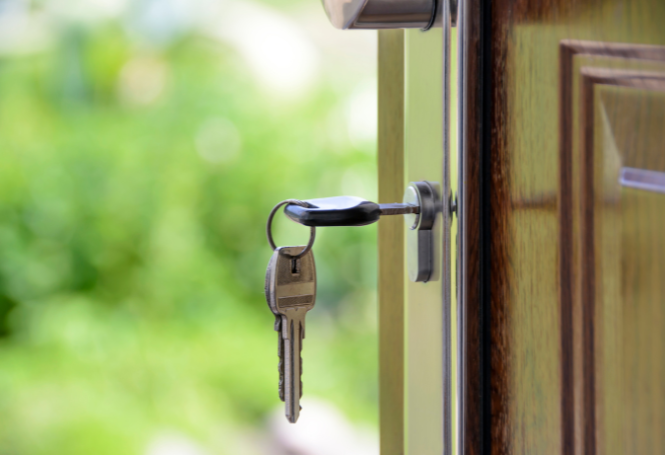 House keys hanging from a door lock with a blurred green background.